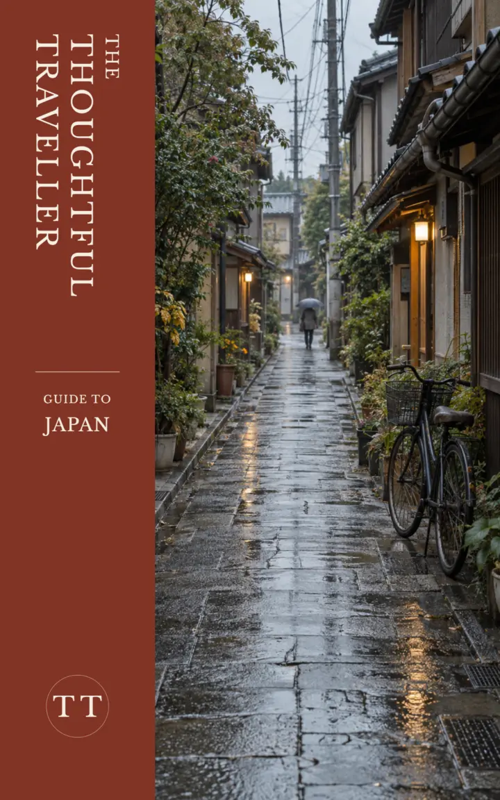 Draft cover of The Thoughtful Traveller Guide to Japan, showing a rainy Japanese backstreet, bicycle and distant umbrella figure beside a rust-coloured title band